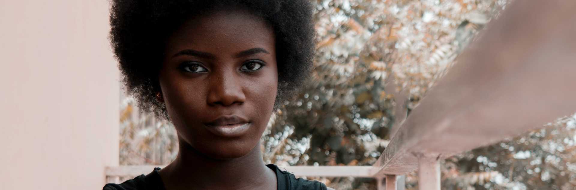 Une jeune personne à l'extérieur faisant directement face à la caméra, avec des arbres flous en arrière-plan.