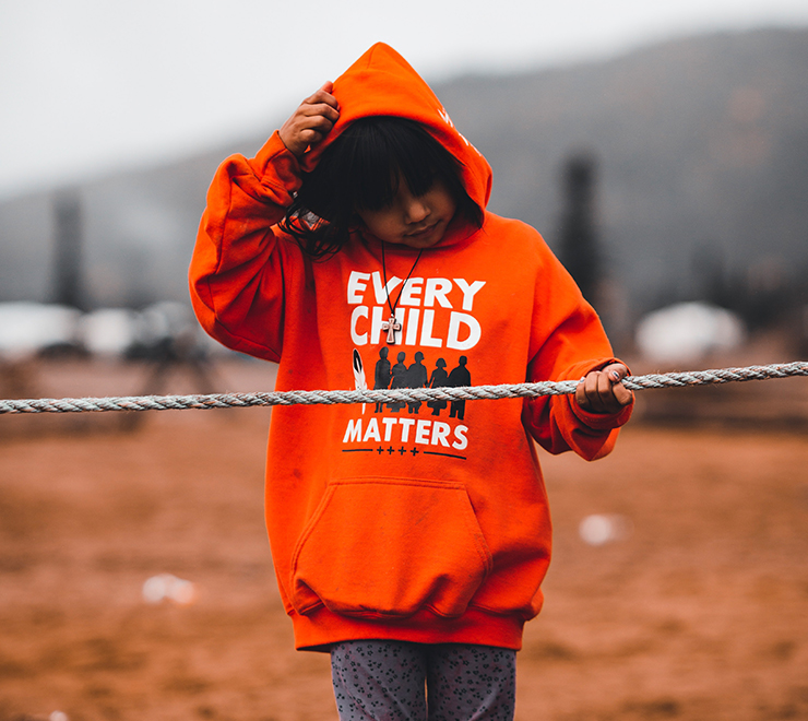 Une jeune personne portant une veste à capuchon orange sur laquelle est écrit « Every Child Matters » (Chaque enfant compte)