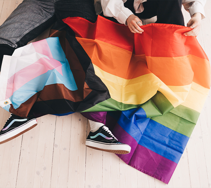 Deux jeunes personnes assises par terre, tenant un drapeau de la fierté sur leurs genoux