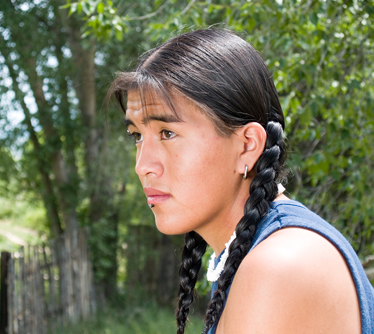Un·e jeune Autochtone portant des tresses avec des arbres en arrière-plan